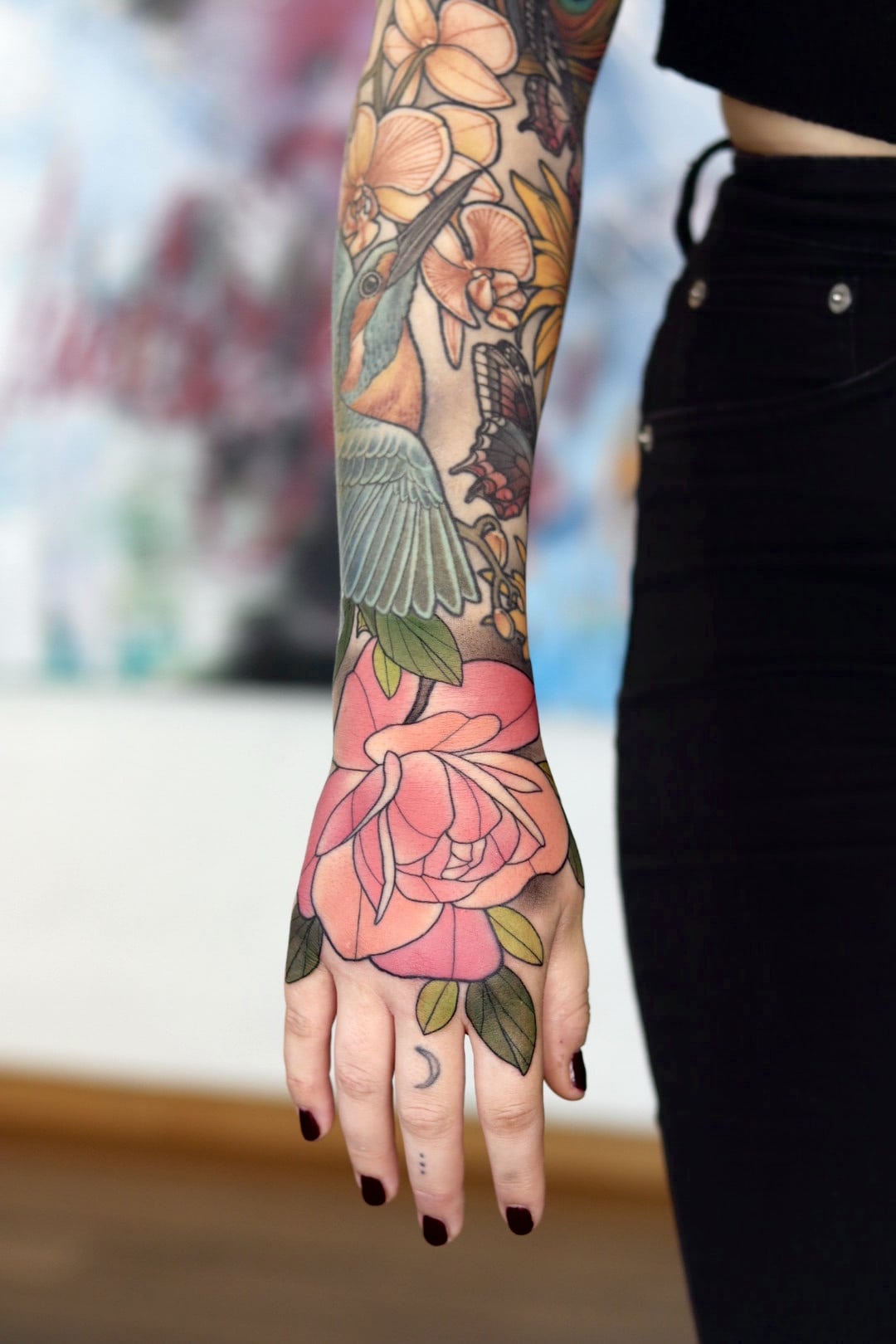 Neotraditional tatuering i färg på en underarm och ner över handen av växter i grönt och rosa.